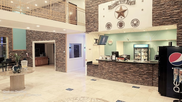 A lobby with a reception desk, a Pepsi refrigerator, and a stone wall with military insignia. - B&J Hotel and Apartment (Pecos)