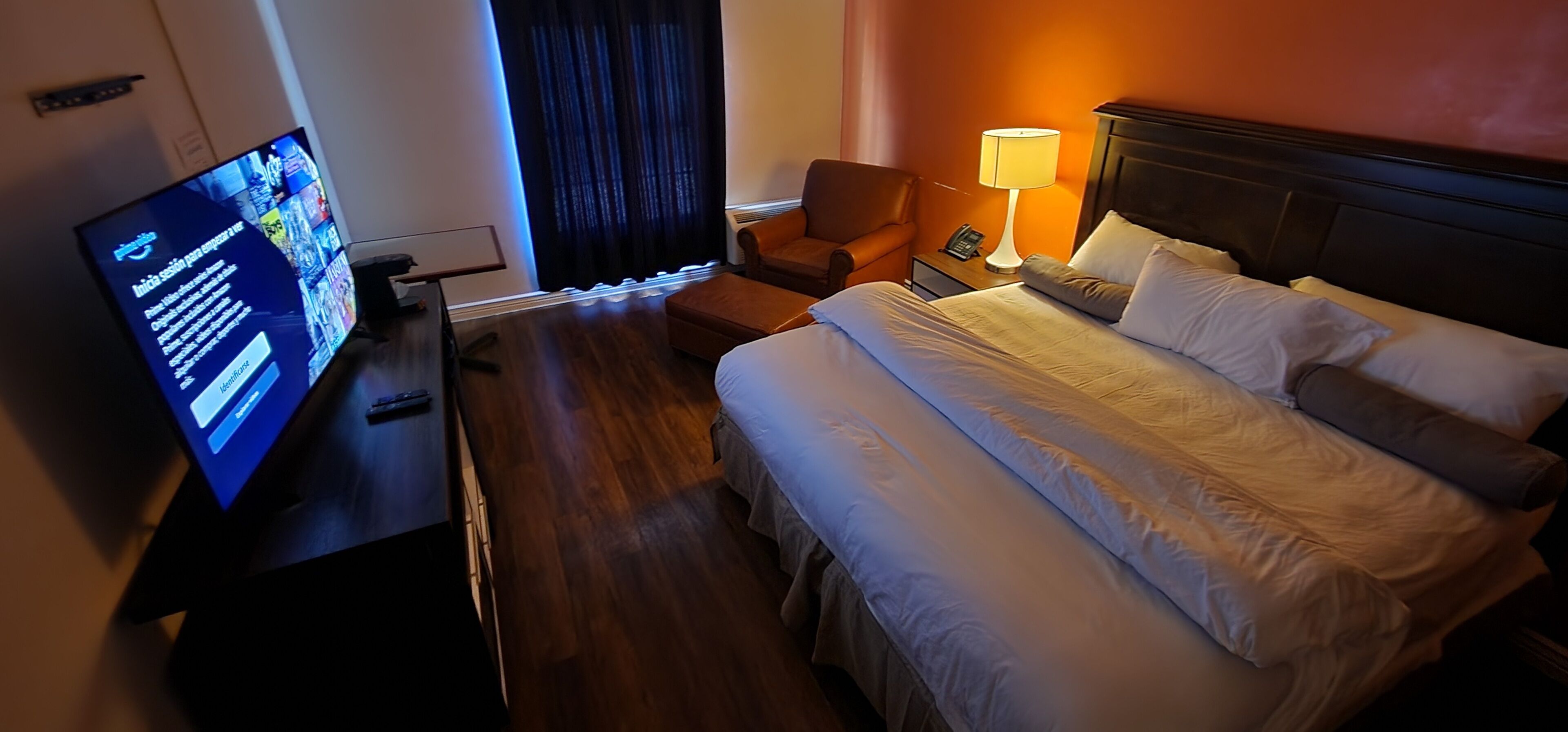 Una habitación de hotel con cama, una silla, un escritorio con computadora, televisión y lámpara.