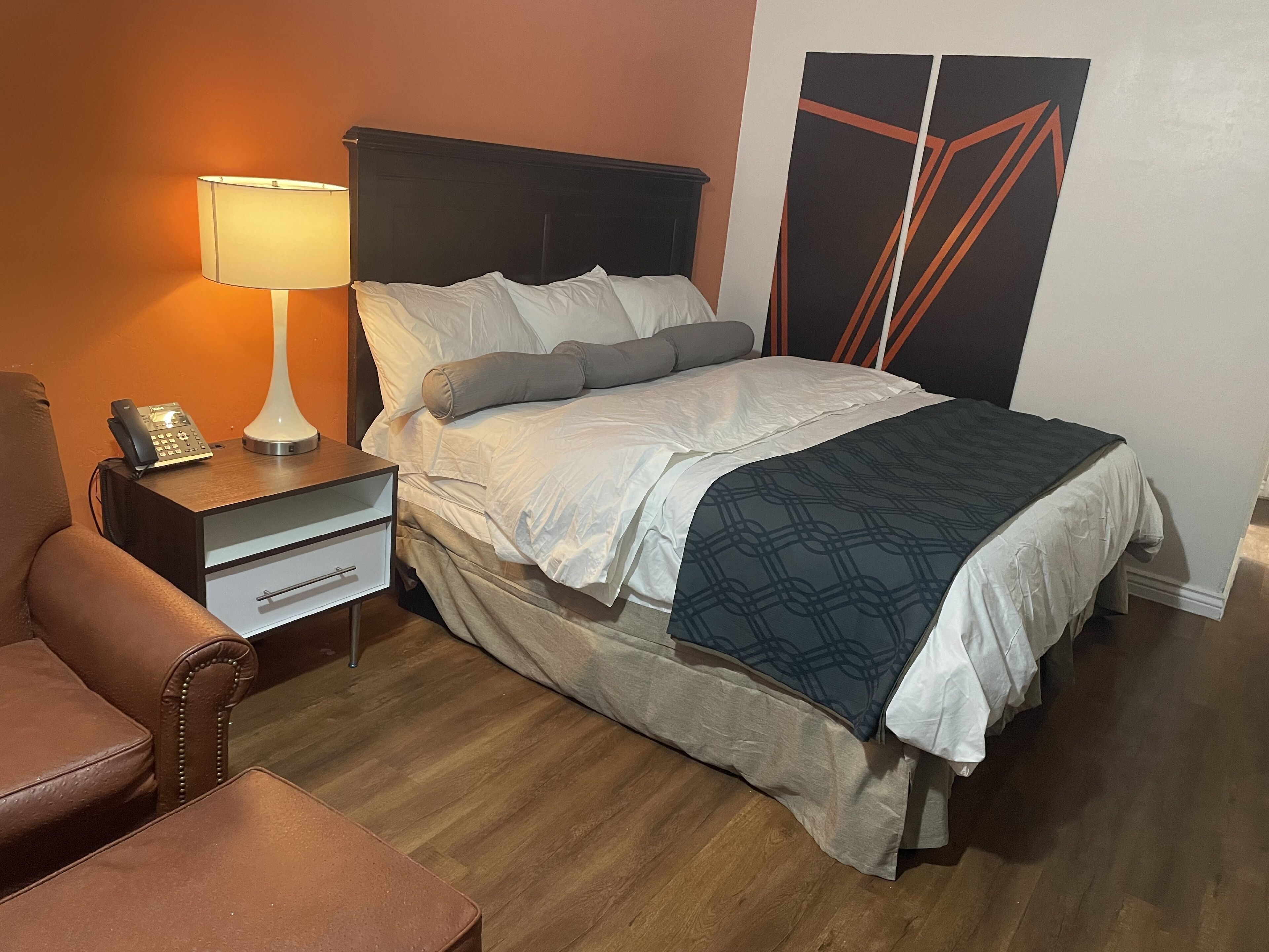 Un lit bien fait, avec une couette grise et blanche, une table de chevet avec une lampe, un téléphone et un fauteuil en cuir marron.