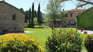 Une cour avec un bâtiment en briques, une pelouse bien entretenue et un arbre.