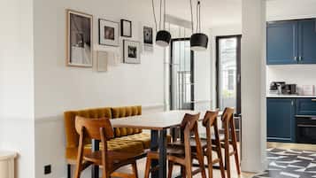 Un'area pranzo con tavolo e sedie in legno, un divano color senape e lampade a sospensione nere.