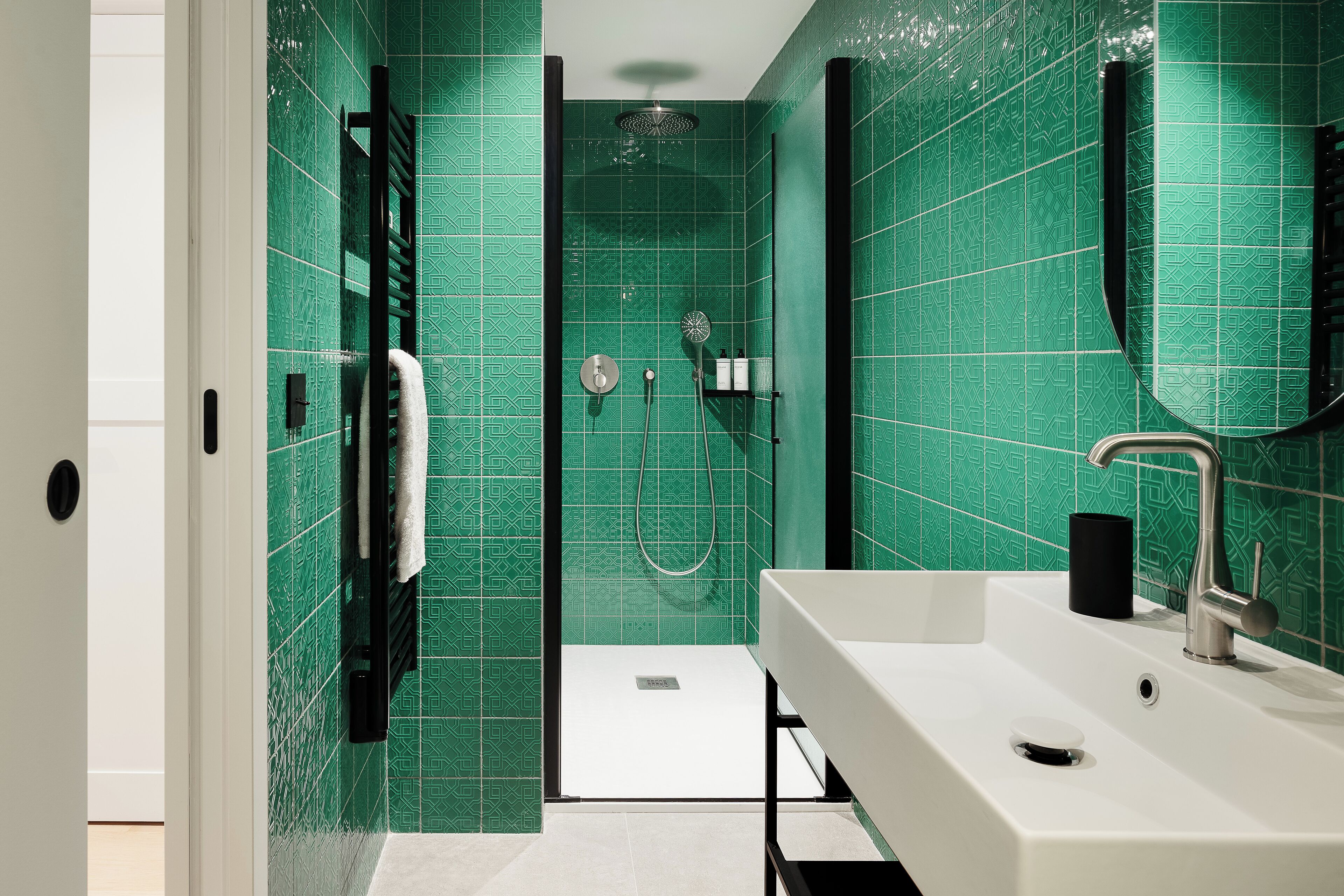 A modern bathroom with green tiled walls, a white sink, and a shower area.