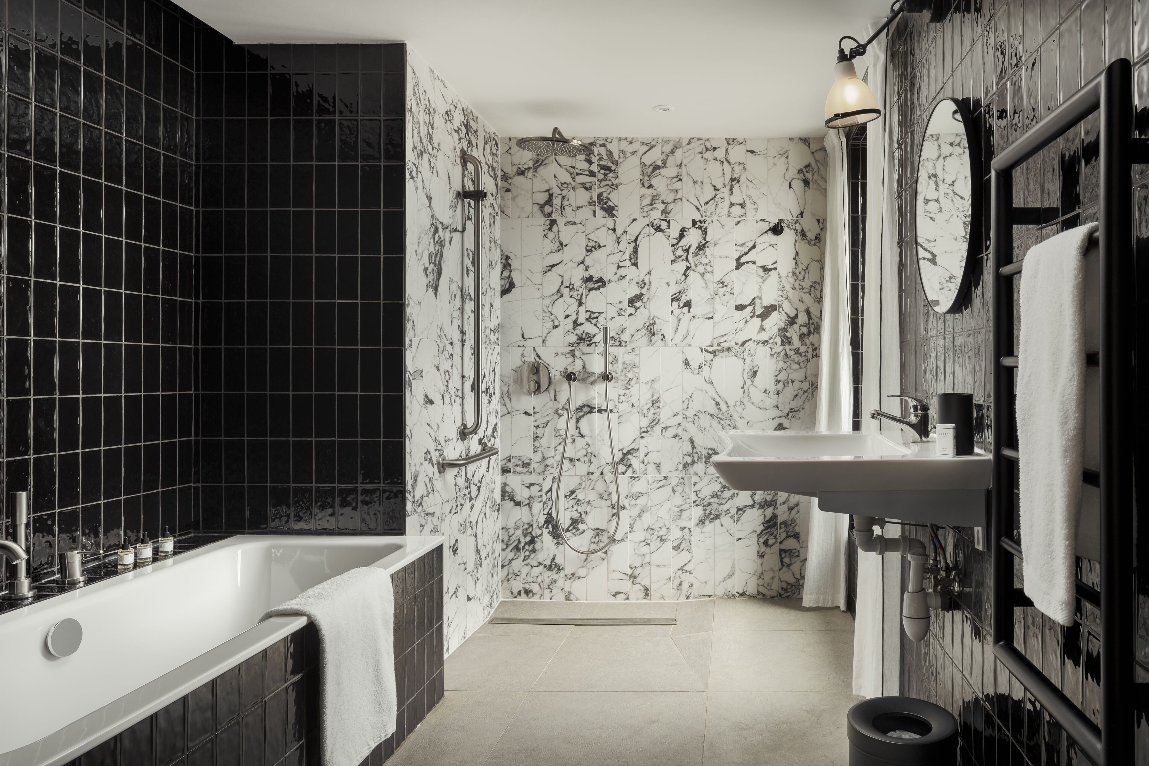A modern bathroom with a freestanding bathtub, a shower with a glass door, a sink with a mirror, and black and white patterned tiles.