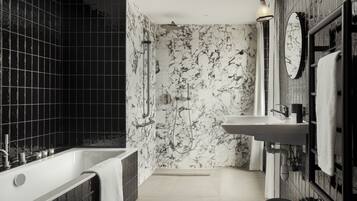 A modern bathroom with a freestanding bathtub, a shower with a glass door, a sink with a mirror, and black and white patterned tiles.