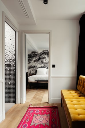 A modern bedroom with a bed, a yellow tufted bench, a patterned rug, and a wall mural.