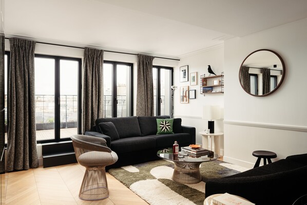 A modern living room with a black sofa, a round coffee table, and a large window with curtains. - My Maison In Paris - Invalides (Paris)