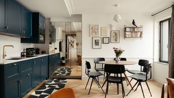 A modern kitchen with dark blue cabinets, a black and white patterned rug, and a dining area with black chairs and a round table.