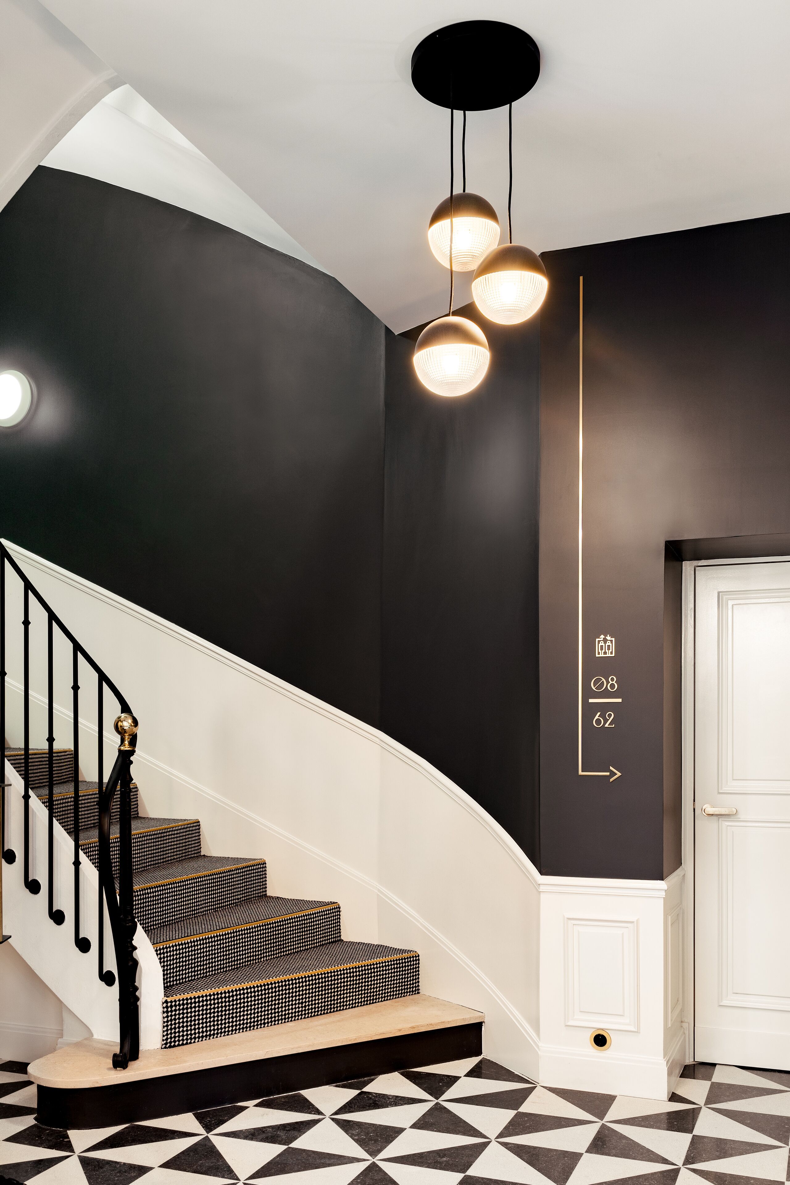 A staircase with black and white patterned steps, a black wall, and a white door with a number sign.
