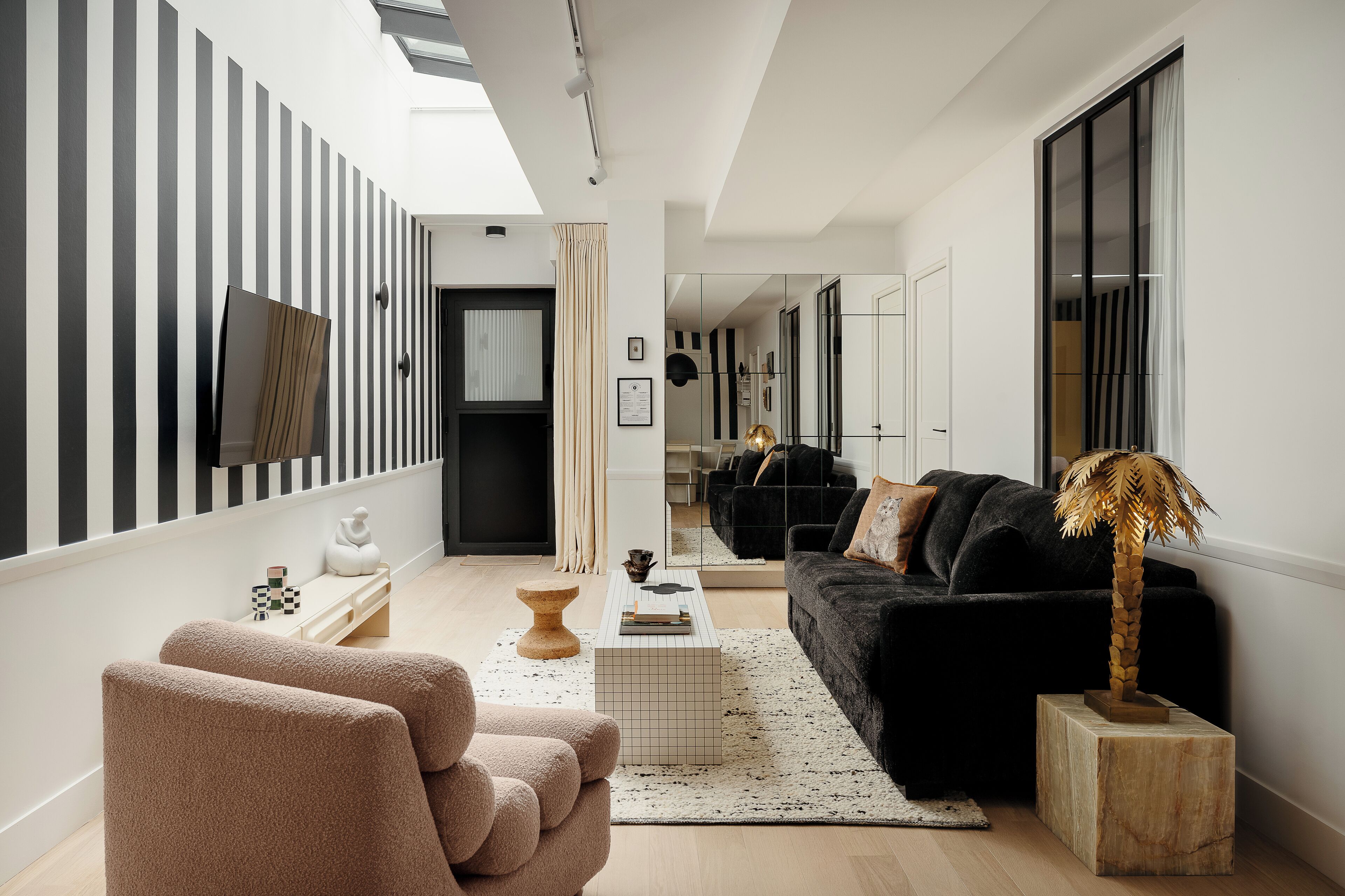 Un salon moderne avec un canapé noir, une table basse en bois et une sculpture originale représentant un palmier.