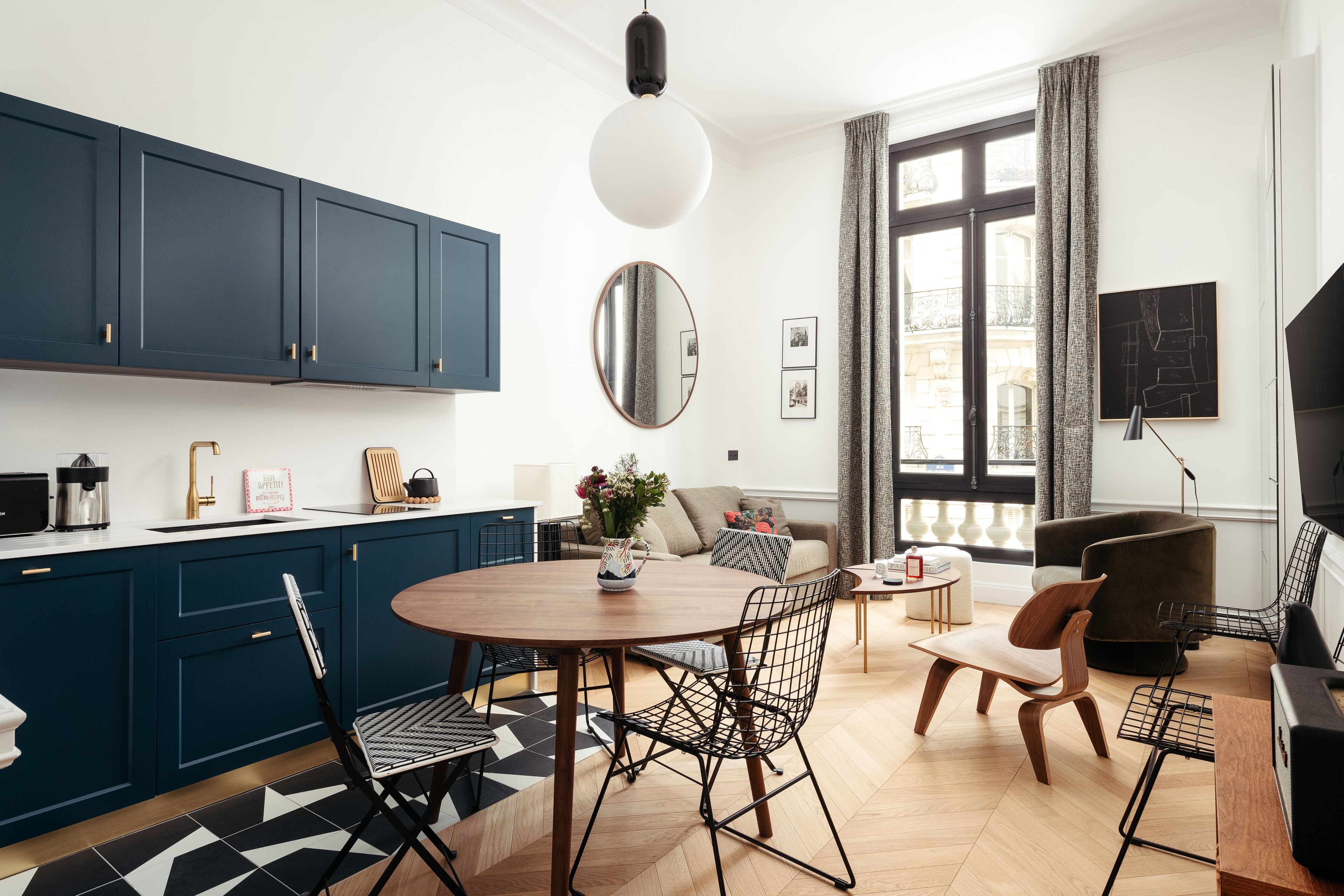 A modern kitchen with dark blue cabinets, a round dining table, and a mix of modern and classic chairs.