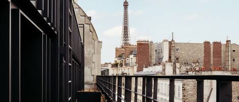 A wooden walkway with metal railings, leading to a view of the Eiffel Tower and surrounding buildings.