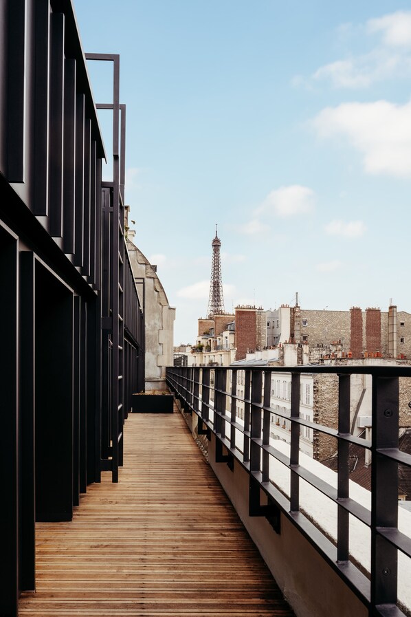 A wooden walkway with metal railings, leading to a view of the Eiffel Tower and surrounding buildings.