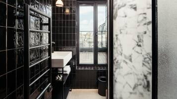 A modern bathroom with black tiled walls, a white sink, and a window with a view of buildings.