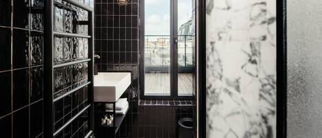 A modern bathroom with black tiled walls, a white sink, and a window with a view of buildings.