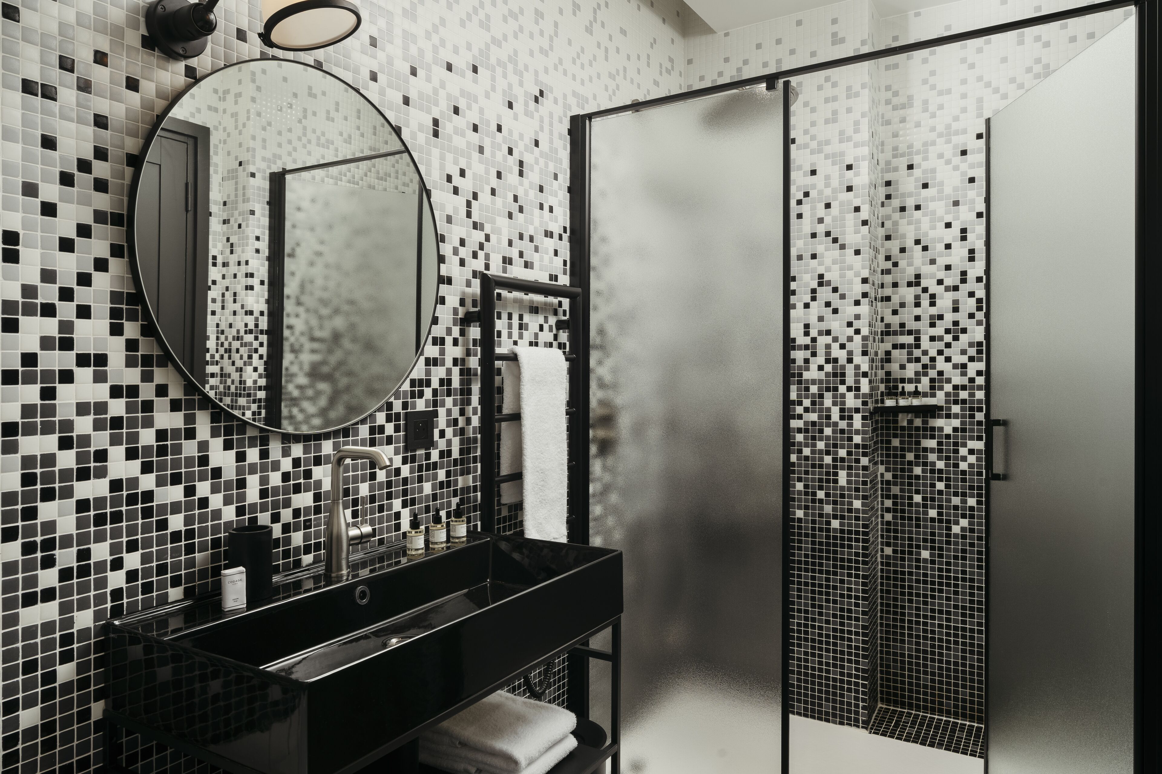 A modern bathroom with a black sink, a round mirror, and a tiled shower area.