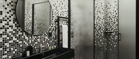 A modern bathroom with a black sink, a round mirror, and a tiled shower area.