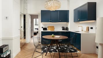 Cozinha moderna com armários azul escuro, uma mesa redonda de madeira e cadeiras de arame pretas.