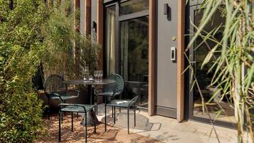 An outdoor patio with a table and chairs, surrounded by greenery and a modern building facade.