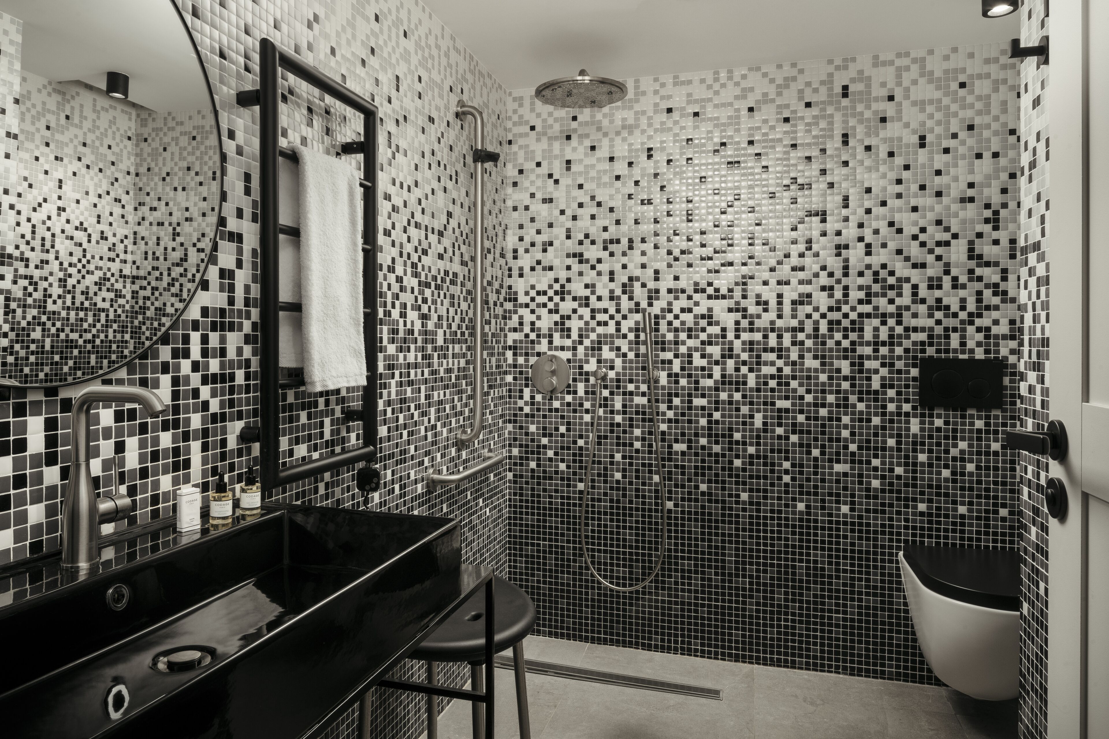 A modern bathroom with a black sink, a mirror, and a shower area with mosaic tile walls.