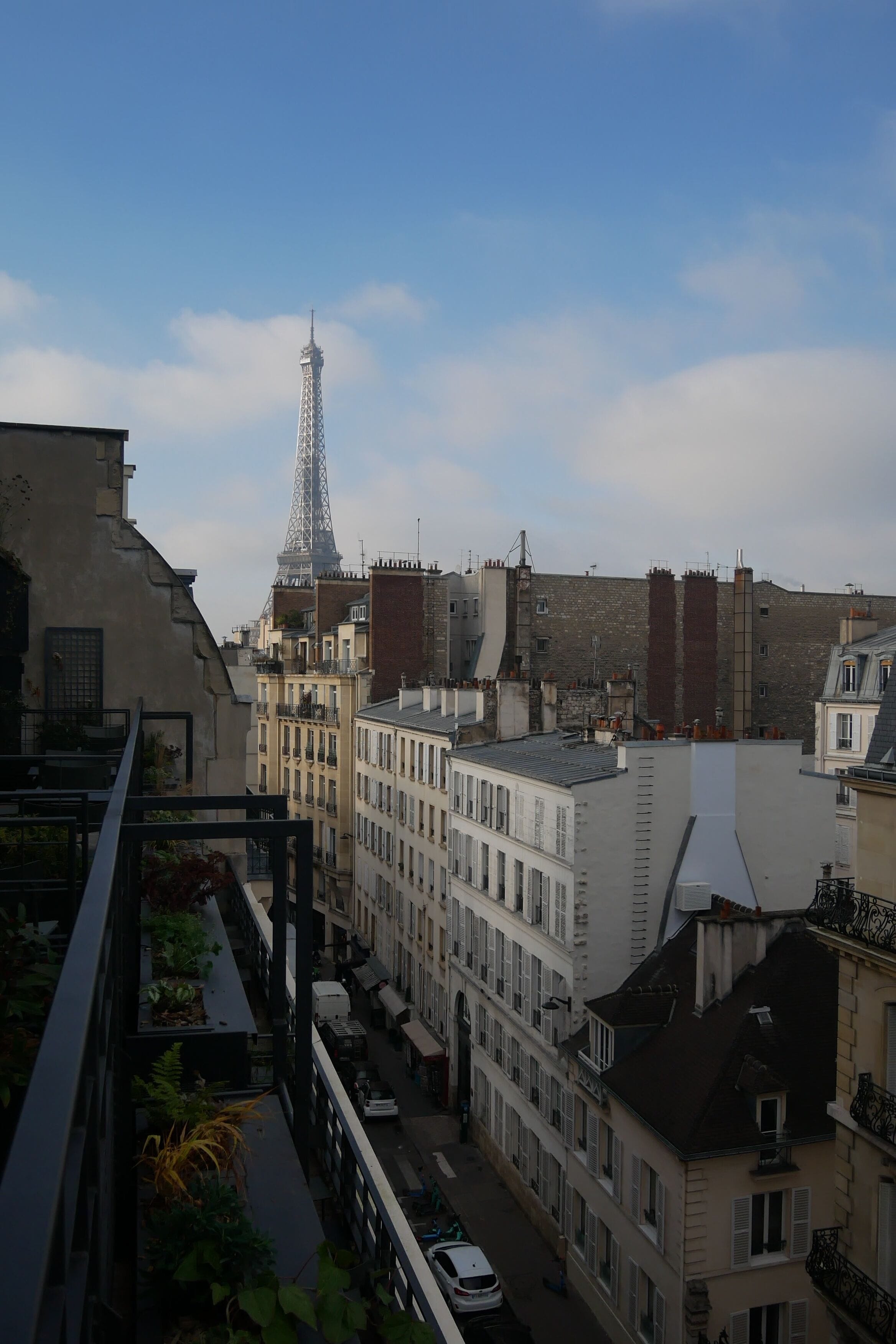 Une vue de Paris avec la Tour Eiffel en arrière-plan, entourée de bâtiments historiques et d’une rue étroite.