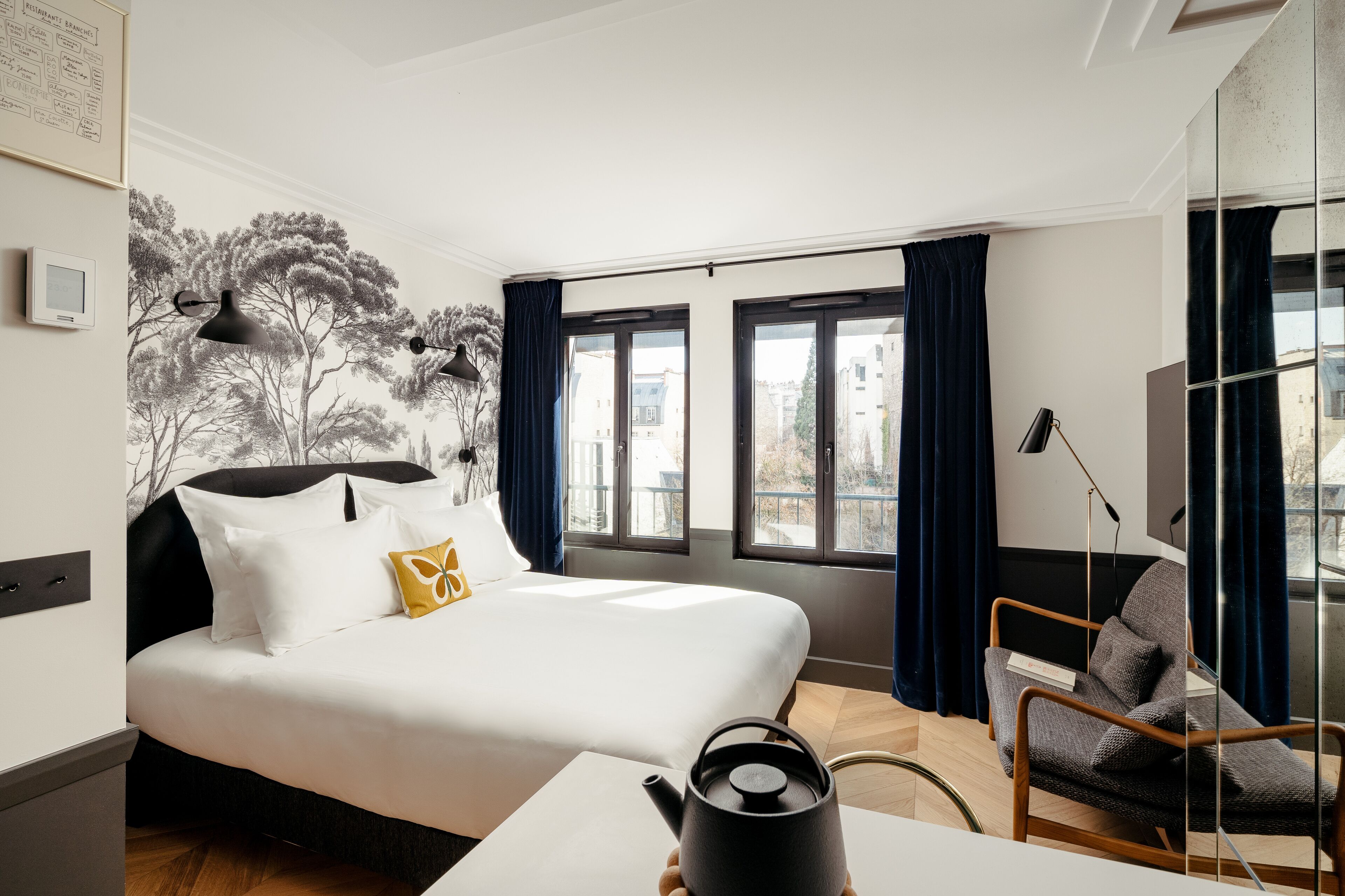 Habitación de hotel moderna con una cama grande, un escritorio, una silla y vistas de la ciudad a través de amplios ventanales.