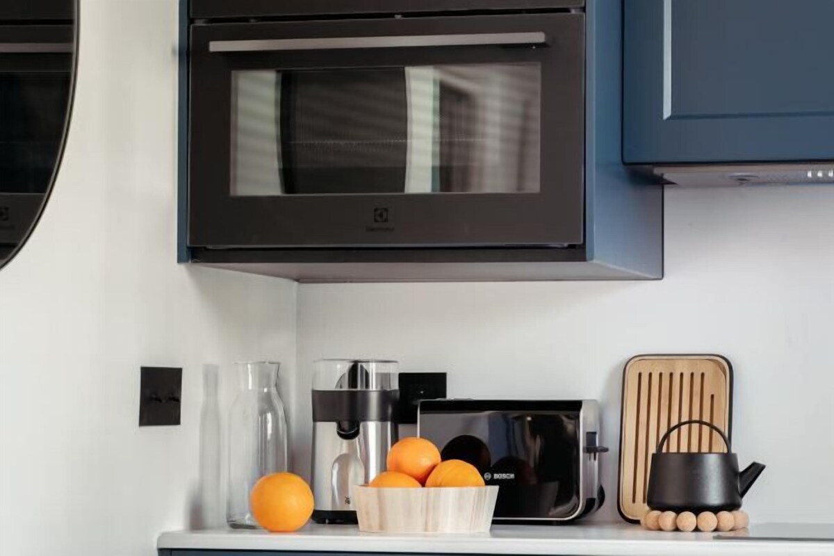 A kitchen with a Bosch microwave, a coffee maker, a toaster, and a wooden cutting board with a black kettle.