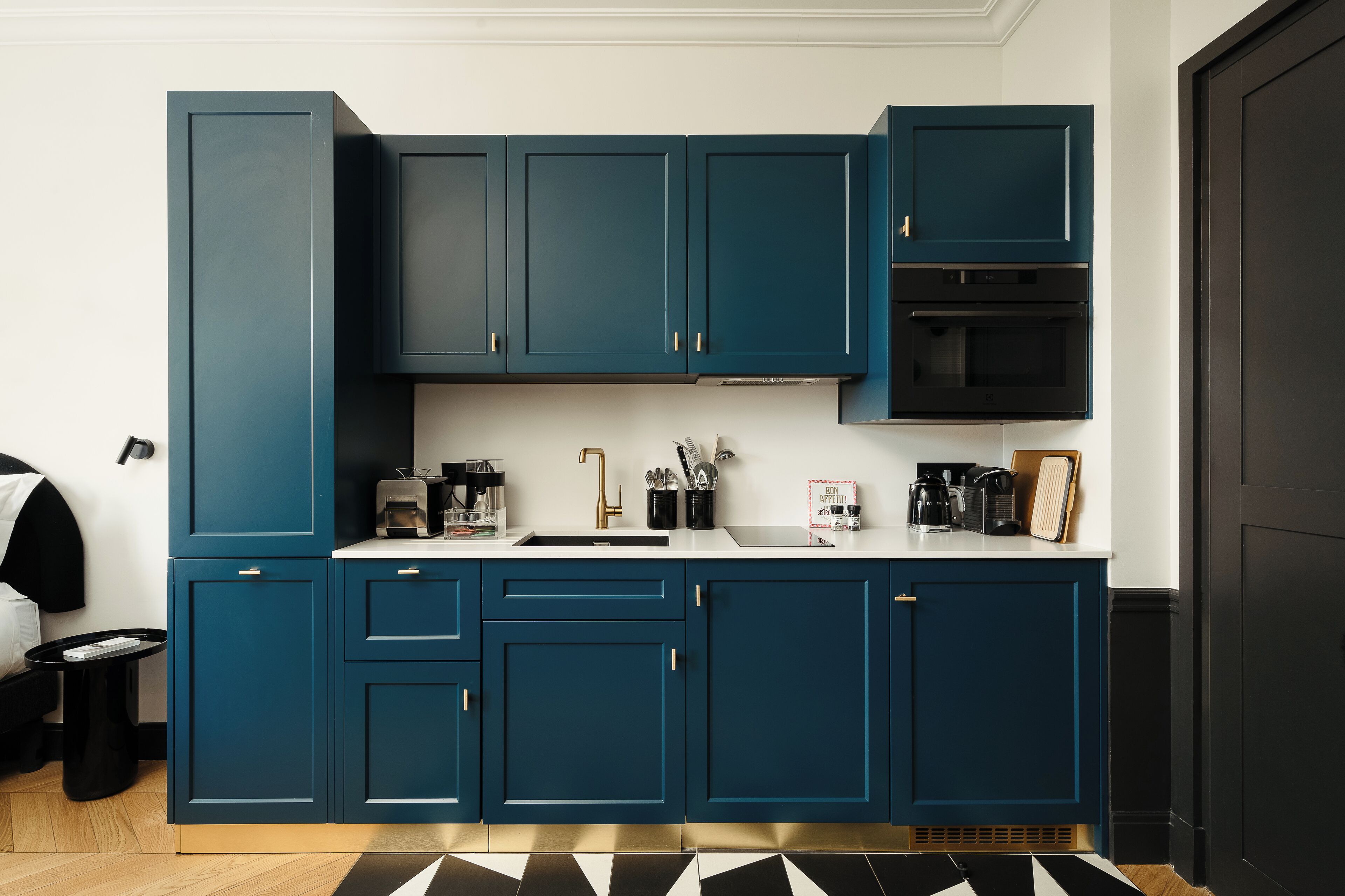 Une cuisine moderne avec des meubles bleu foncé, un four noir et un plan de travail blanc.