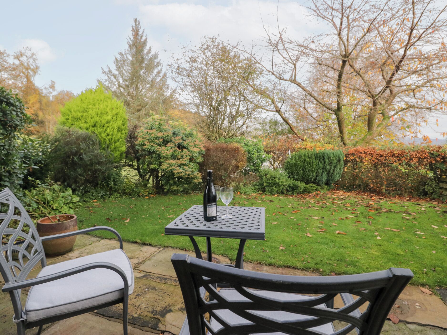 A patio with a table and two chairs, surrounded by a well-maintained garden with various shrubs and trees.