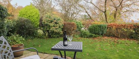 A patio with a table and two chairs, surrounded by a well-maintained garden with various shrubs and trees.