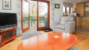 Un salon équipé d’un téléviseur, d’un canapé, d’une table basse et d’une porte-fenêtre coulissante donnant sur un jardin.