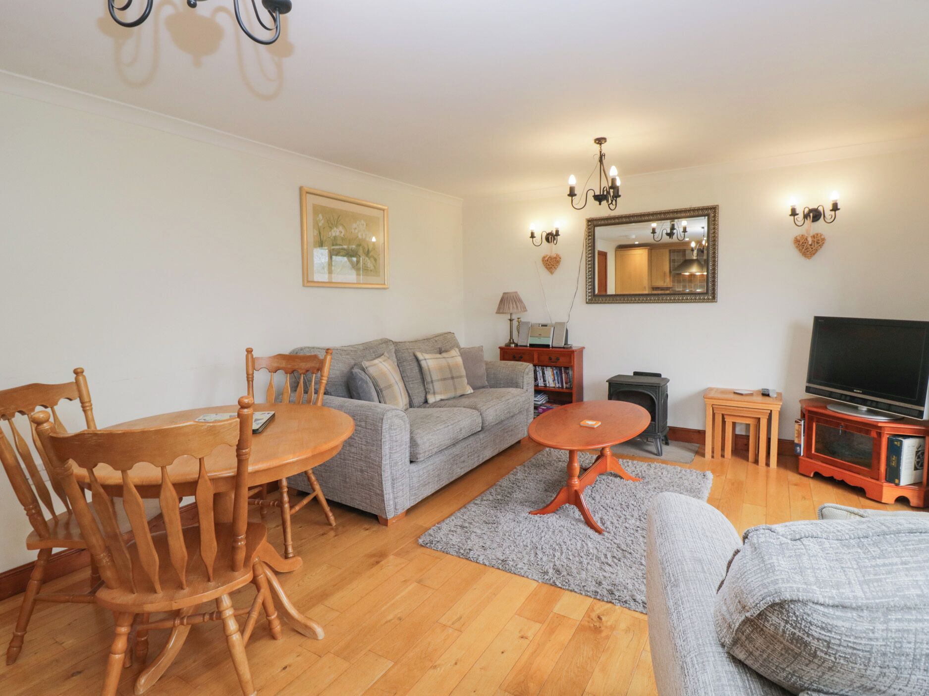 A living room with a sofa, wooden chairs, a small table, a television, and a fireplace.