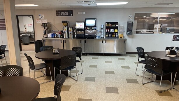 A cafeteria with tables and chairs, a coffee machine, and a refrigerator. - The Armadillo Hotel Carlsbad (Carlsbad)