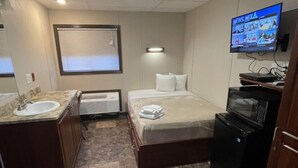 A compact hotel room with a bed, a small desk, a TV, a microwave, and a bathroom with a sink and mirror. - The Armadillo Hotel Carlsbad (Carlsbad)