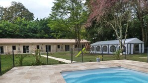 Una piscina con un deck de azulejos, un patio cercado y un edificio con techo de tejas al fondo.