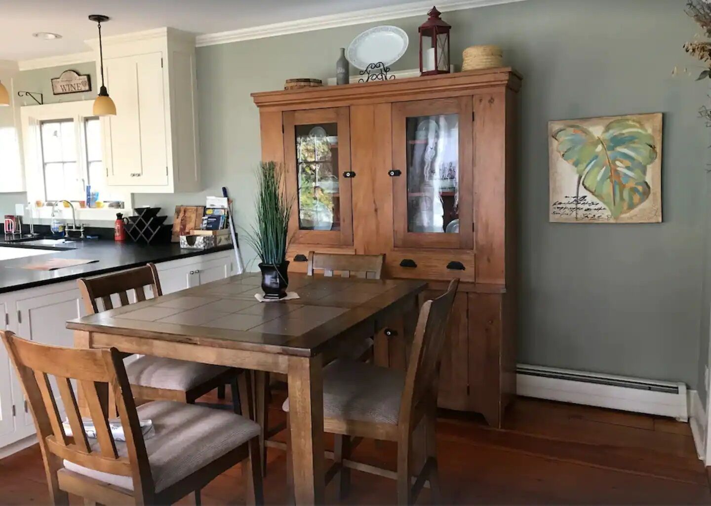 Un coin repas avec une table et des chaises en bois, un buffet avec des portes en verre, et une cuisine en arrière-plan.