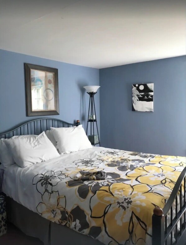 A bedroom with a bed, a floor lamp, and two wall art pieces.
