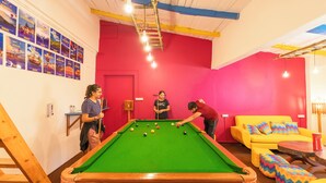 Ein Billardtisch in einem hell gefärbten Raum mit roter Wand und gelber Couch.