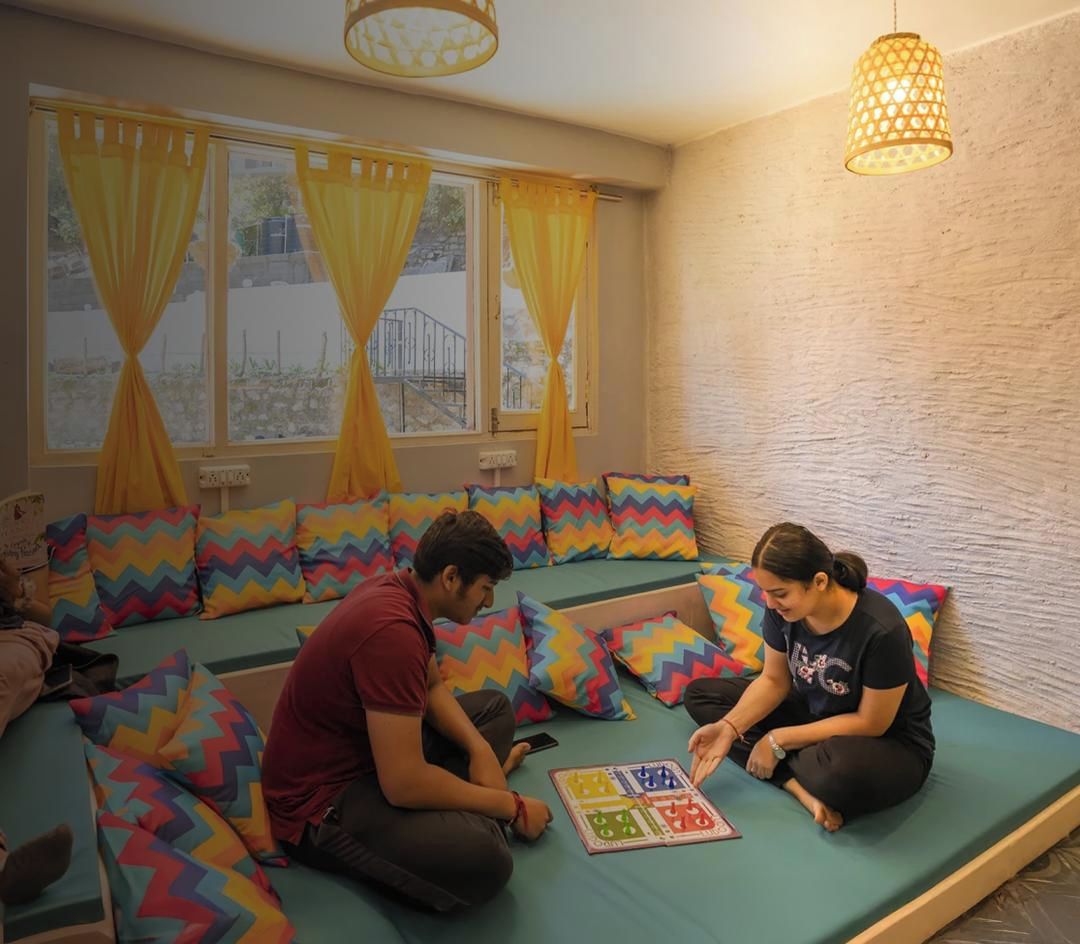 Una habitación con un sofá verde, cojines de estampado zigzag colorido y una ventana con cortinas amarillas.