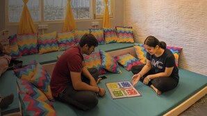A room with a green sofa set, colorful zigzag-patterned cushions, and a window with yellow curtains. - goSTOPS Nainital (Nainital)