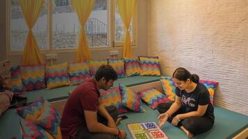 Una habitación con un sofá verde, cojines de estampado zigzag colorido y una ventana con cortinas amarillas.