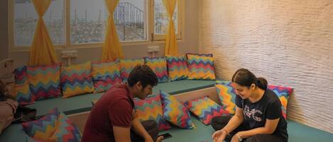 A room with a green sofa set, colorful zigzag-patterned cushions, and a window with yellow curtains.