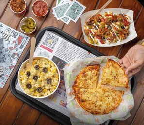 Una bandeja con pizza, pasta y salsas sobre una mesa de madera.
