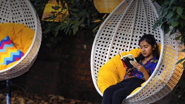 A person sitting in a white wicker swing chair with a yellow cushion, reading a book. - goSTOPS Nainital (Nainital)