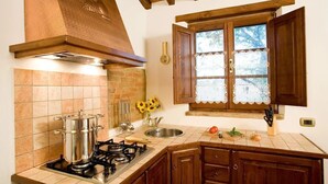 A kitchen with a gas stove, a brick wall, wooden cabinets, and a window with lace curtains.