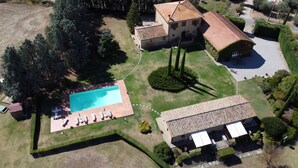 An aerial view of a property with a swimming pool, a large house with a tiled roof, and well-maintained gardens.