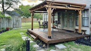 Una terraza de madera con una pérgola, mobiliario exterior y vistas de la casa.