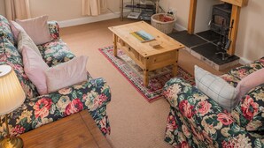 A living room with floral-patterned sofas, a wooden coffee table, a television, and a fireplace. - UK35715 - South Cottage (Howpasley, near Hawick)