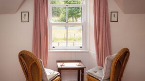 A room with two wicker chairs, a small table, and a window with pink curtains. - UK35715 - South Cottage (Howpasley, near Hawick)