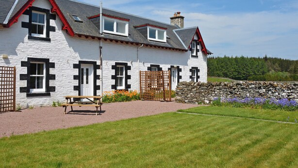 A white building with black window frames and red accents, a stone wall, and a grassy lawn. - UK35715 - South Cottage (Howpasley, near Hawick)