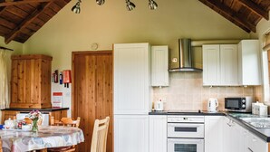 A kitchen with wooden cabinets, a dining table with chairs, and a microwave. - 3 bedroom accommodation in Chelmsford (Chelmsford)